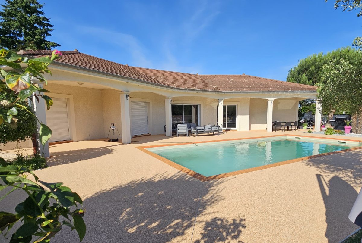 Plage de piscine et terrasse en moquette de pierre beige autour d’une maison de plain-pied