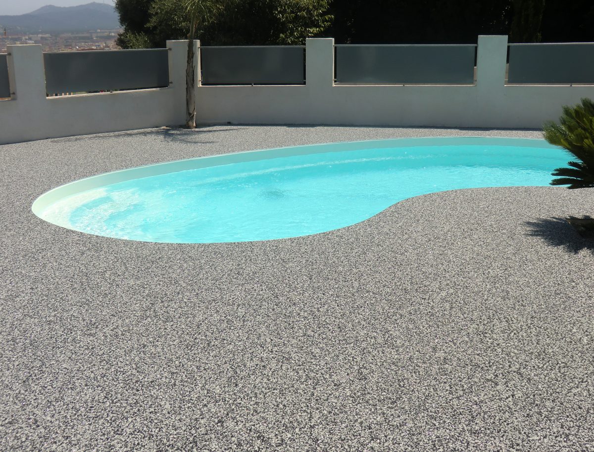 Plage de piscine en moquette de pierre grise autour d’un bassin en forme de haricot